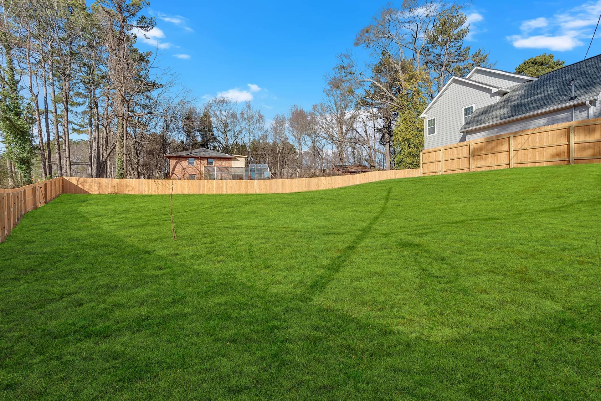 A large lawn with a wooden fence and a house in the background.