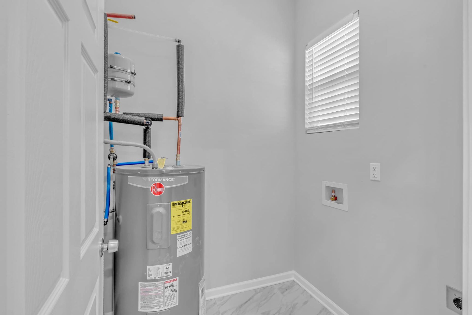 A laundry room with a water heater and a window.