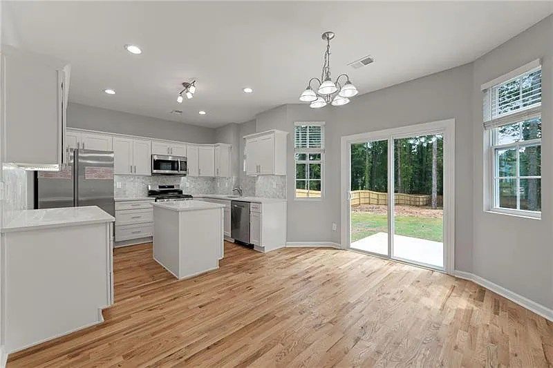 A kitchen with white cabinets , stainless steel appliances , hardwood floors and a sliding glass door.