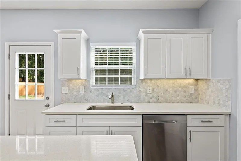 A kitchen with white cabinets , a sink , a dishwasher , and a window.