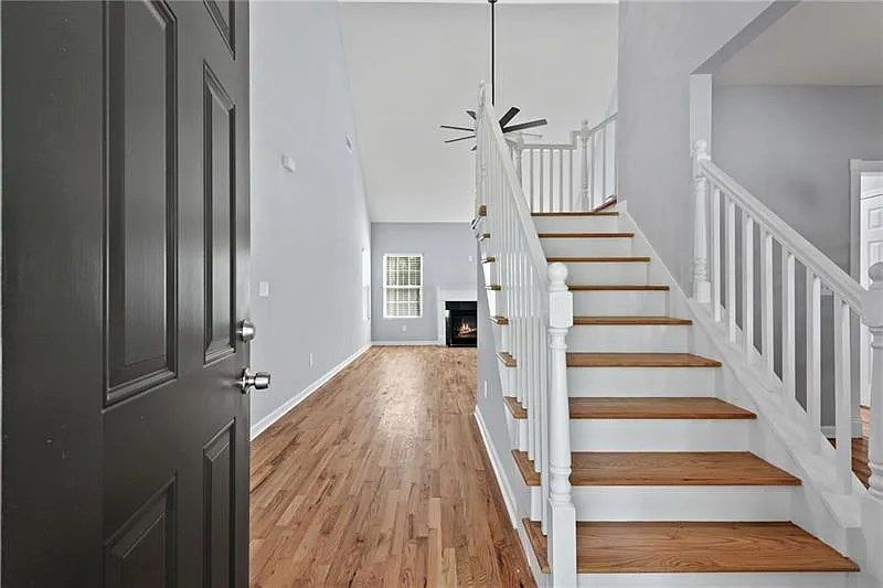 A hallway with hardwood floors and white stairs leading up to the second floor.