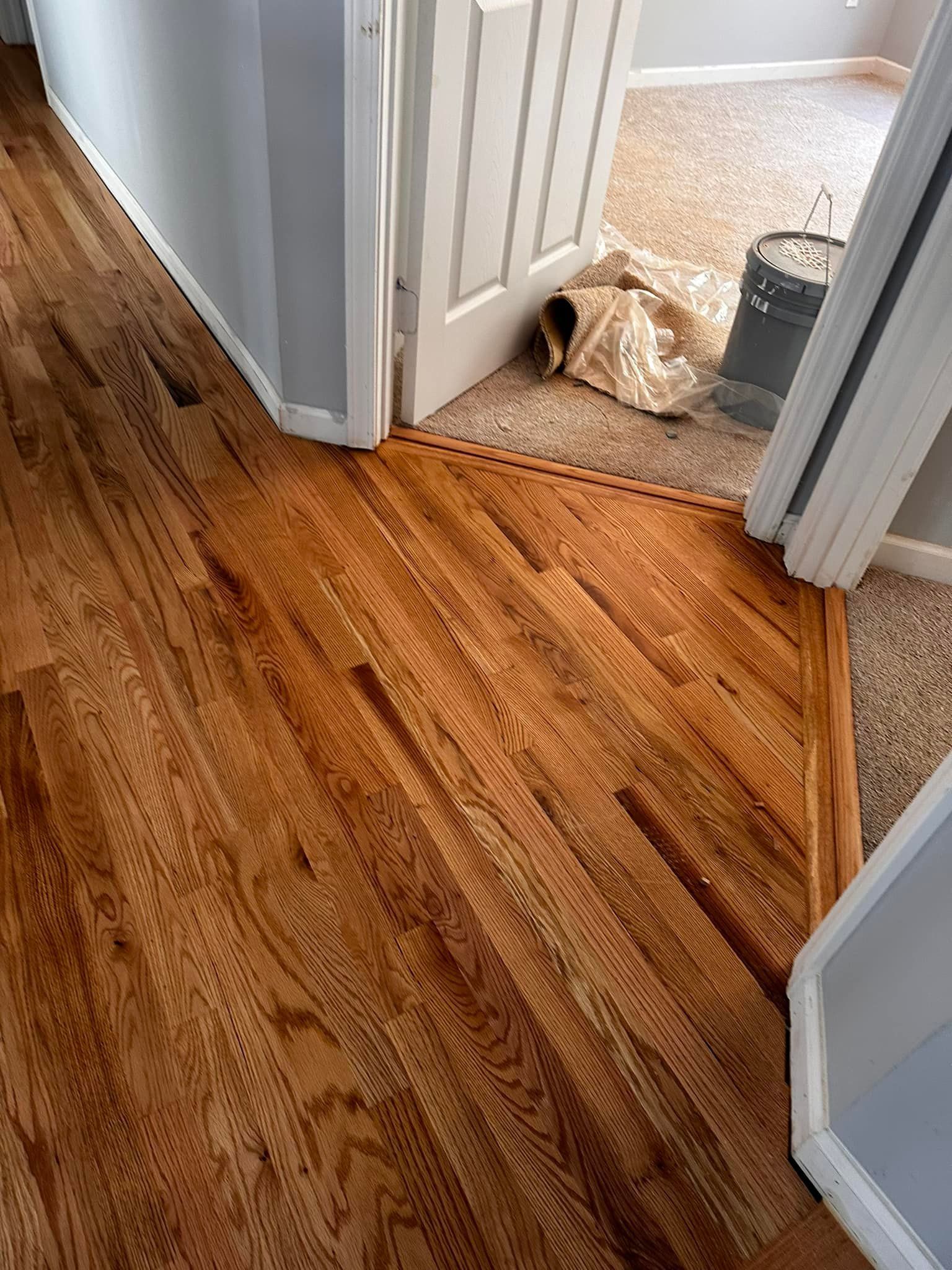 A hallway with hardwood floors and a door leading to a bedroom.