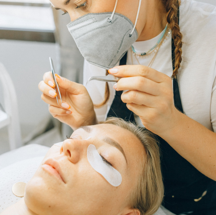A woman wearing a mask is applying eyelash extensions to a woman 's eye