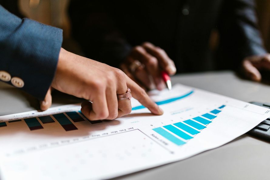 Mãos apontando para um gráfico financeiro com barras azuis, discutindo análise de dados.