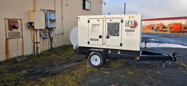 CAT XQ35 35 KWA portable generator Generator on a trailer parked next to a building. The building is beige with rusted electrical boxes.