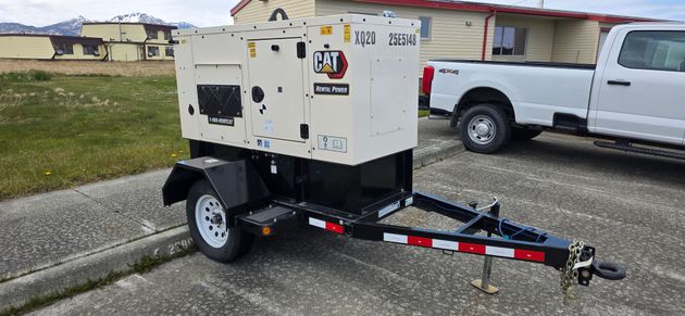 CAT XQ35 35 KWA portable generator Generator on a trailer parked next to a building. The building is beige with rusted electrical boxes.