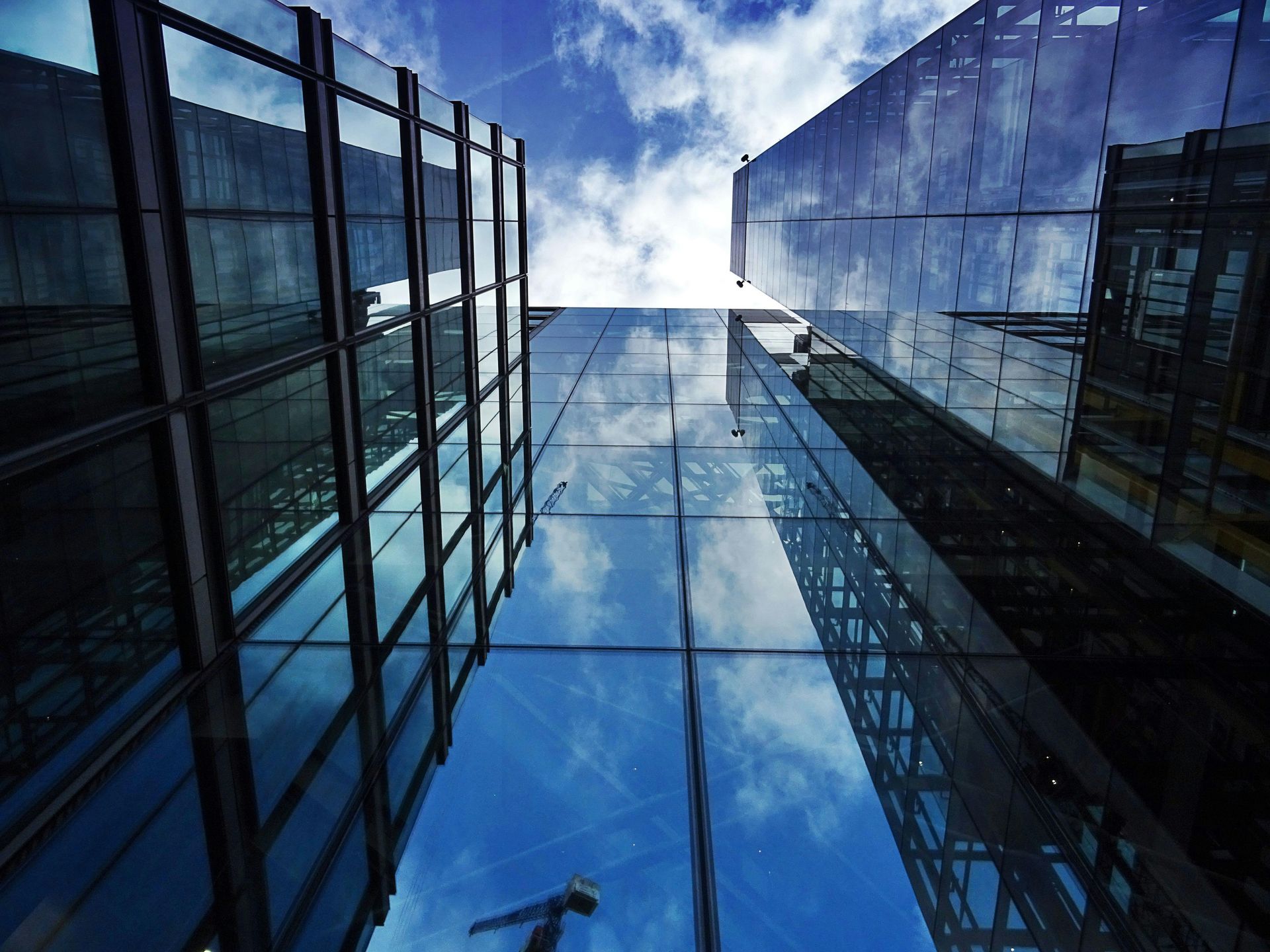 Skyscrapers with glass facades reflect a blue sky with clouds.