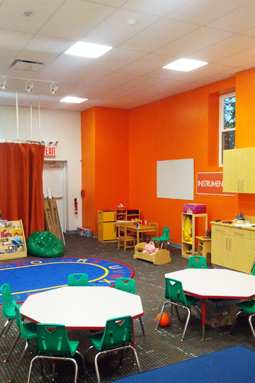 A classroom with orange walls and white tables and chairs