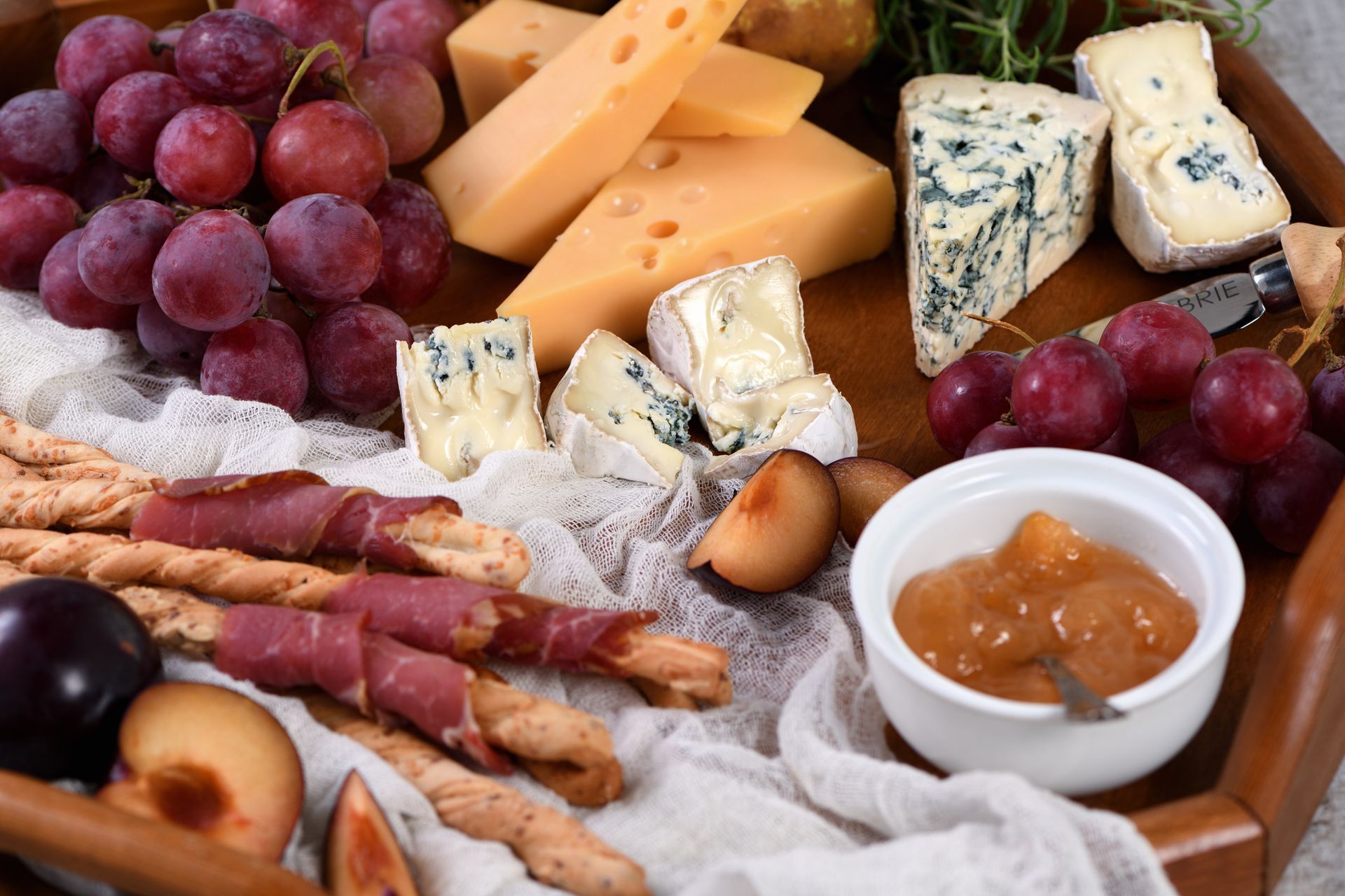Piatto di formaggi e frutta con uva, formaggio, grissini e marmellata di fichi.