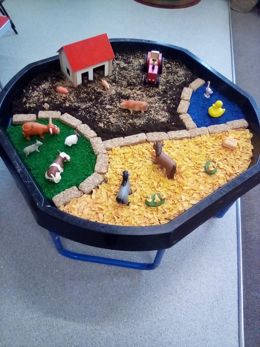 Farm-themed sensory tray with a barn, animals, dirt, grass, water, and food representing farm life.