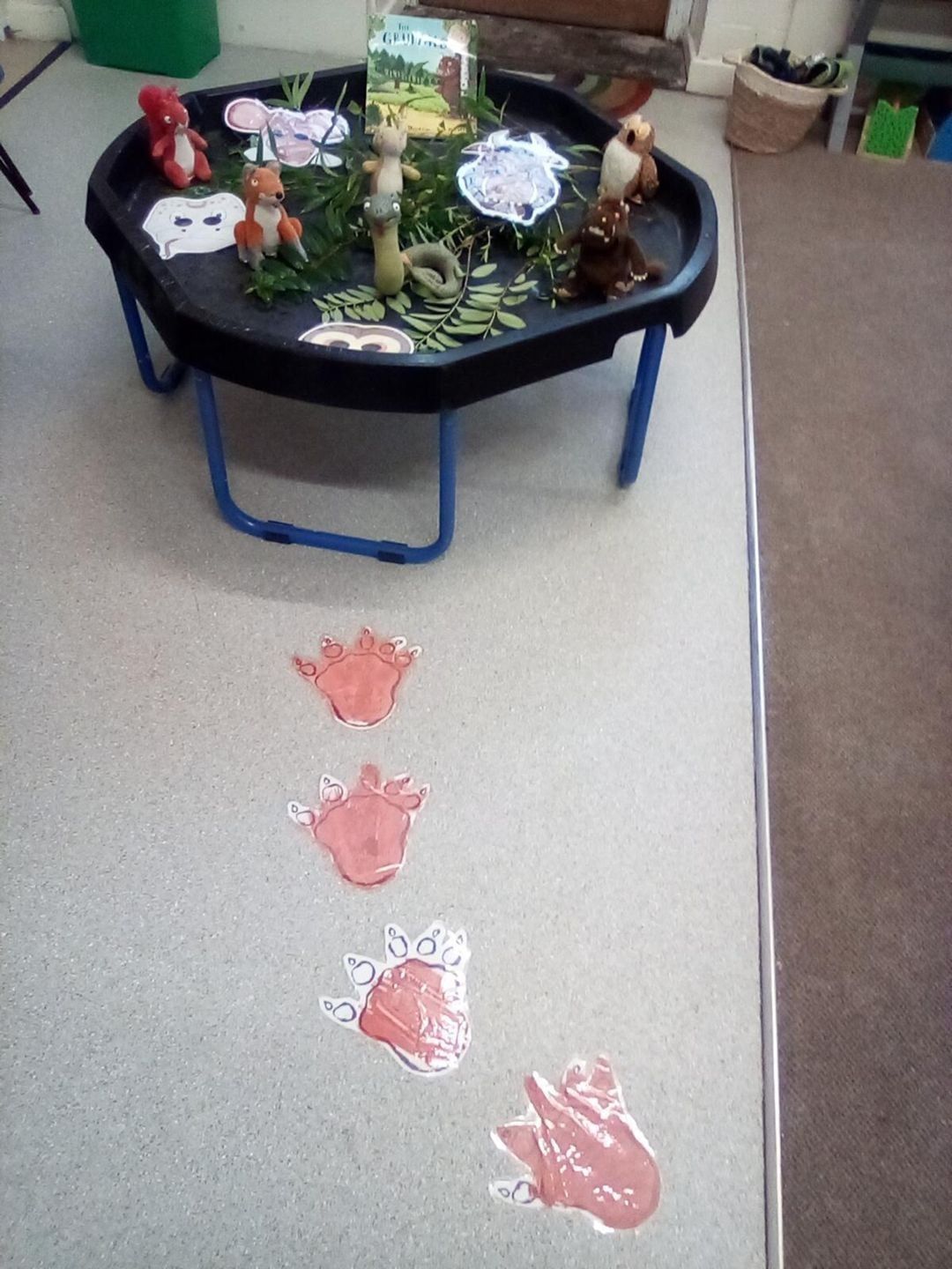 Play tray with toy animals, book, and footprint path on floor.