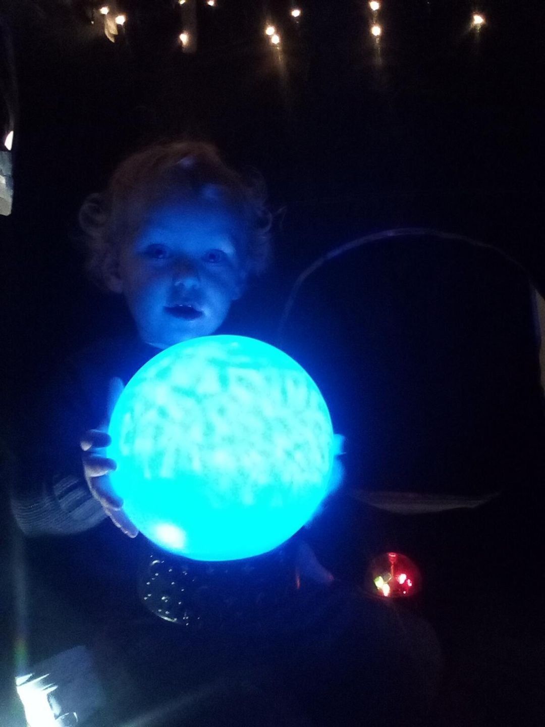 Child holding a glowing blue ball in a dark setting, looking at the light.