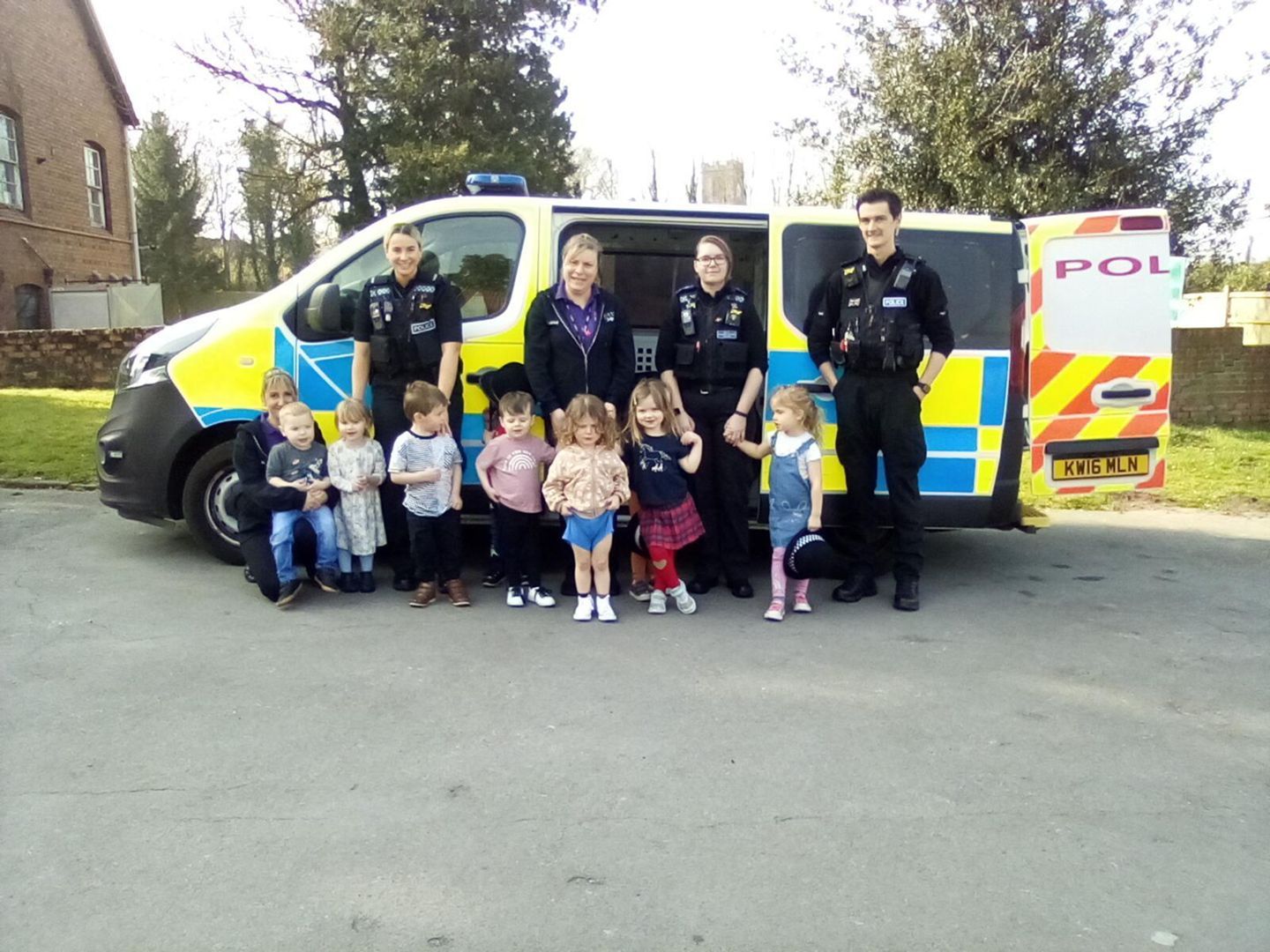 Police officers with children posing by a police van outdoors on a sunny day.