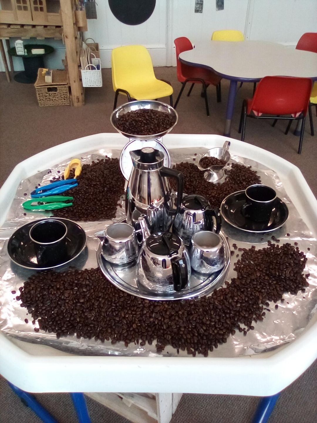 Tray of coffee beans with toy coffee pots, cups, and a scale.