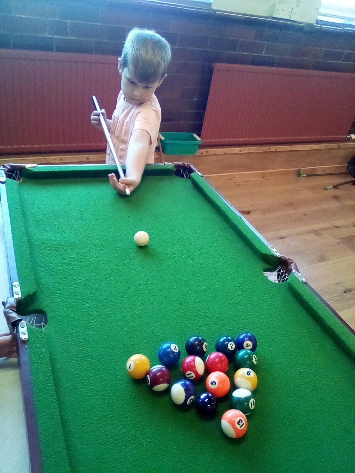 A child aiming a pool cue at a white cue ball on a green pool table.