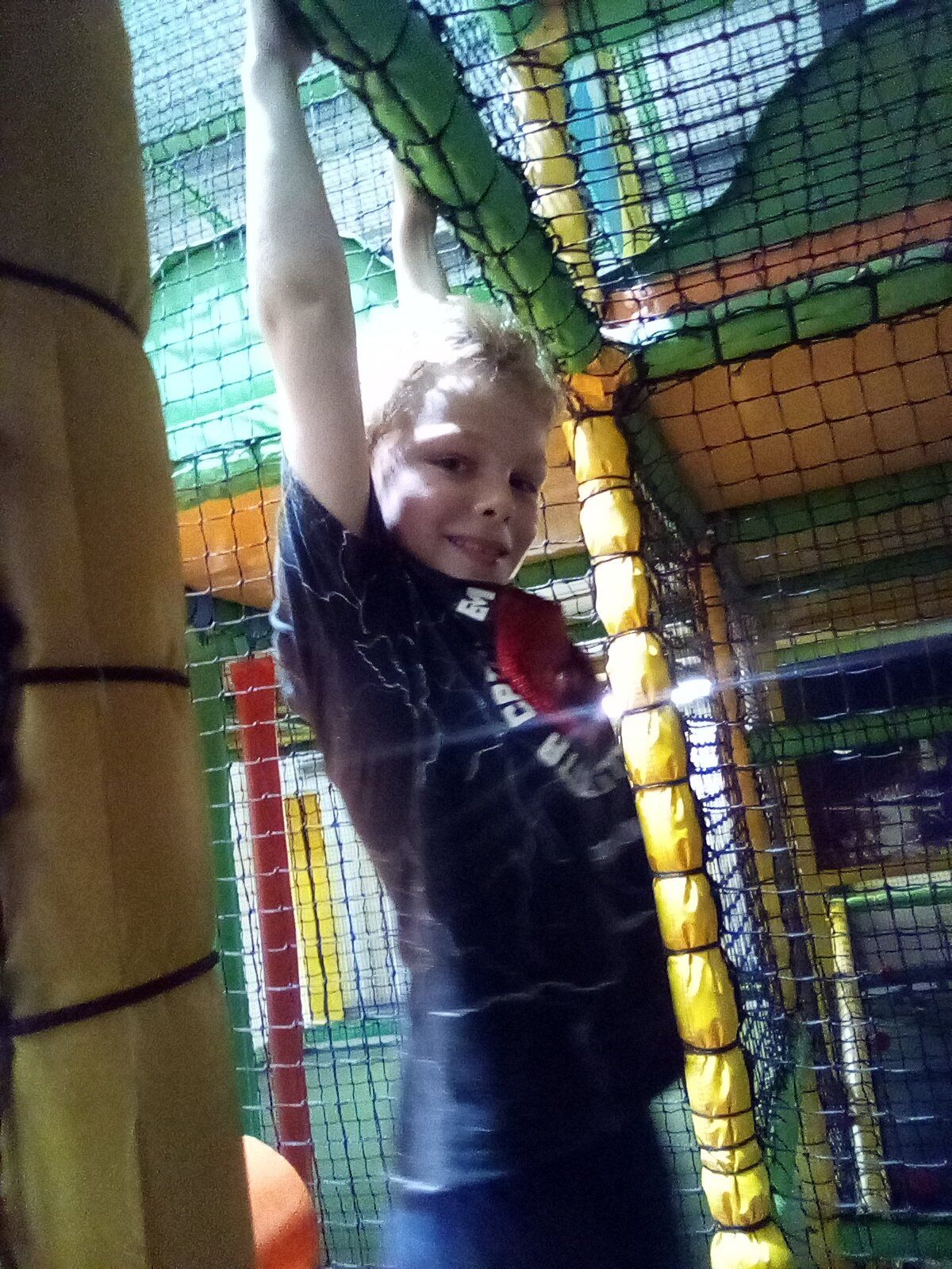Boy hanging from netting in a colorful indoor play structure.