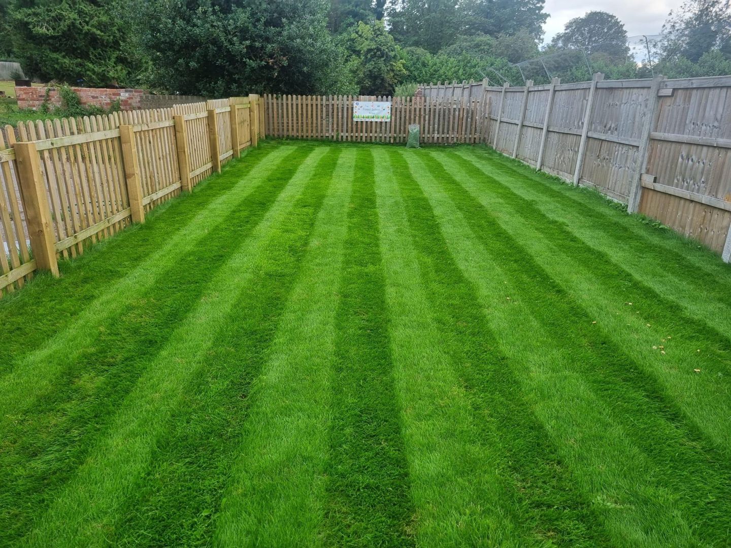 Lawn with striped pattern, framed by wooden fences, green grass, overcast sky.