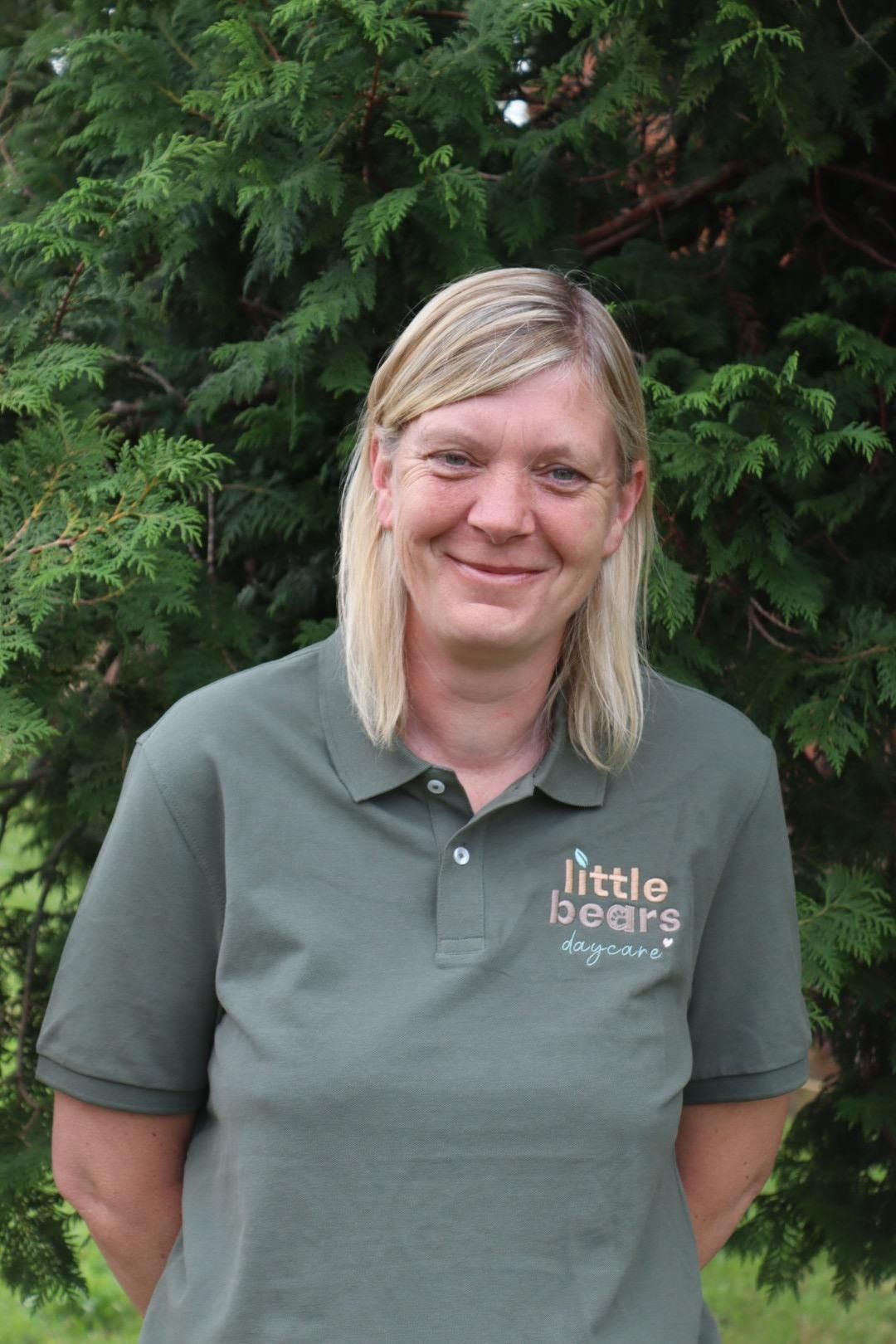 Woman in green polo shirt smiles in front of a green tree. 