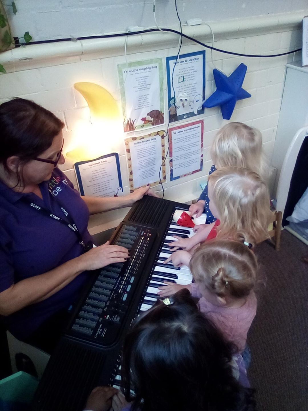 Woman playing keyboard with three children in a room with music posters.