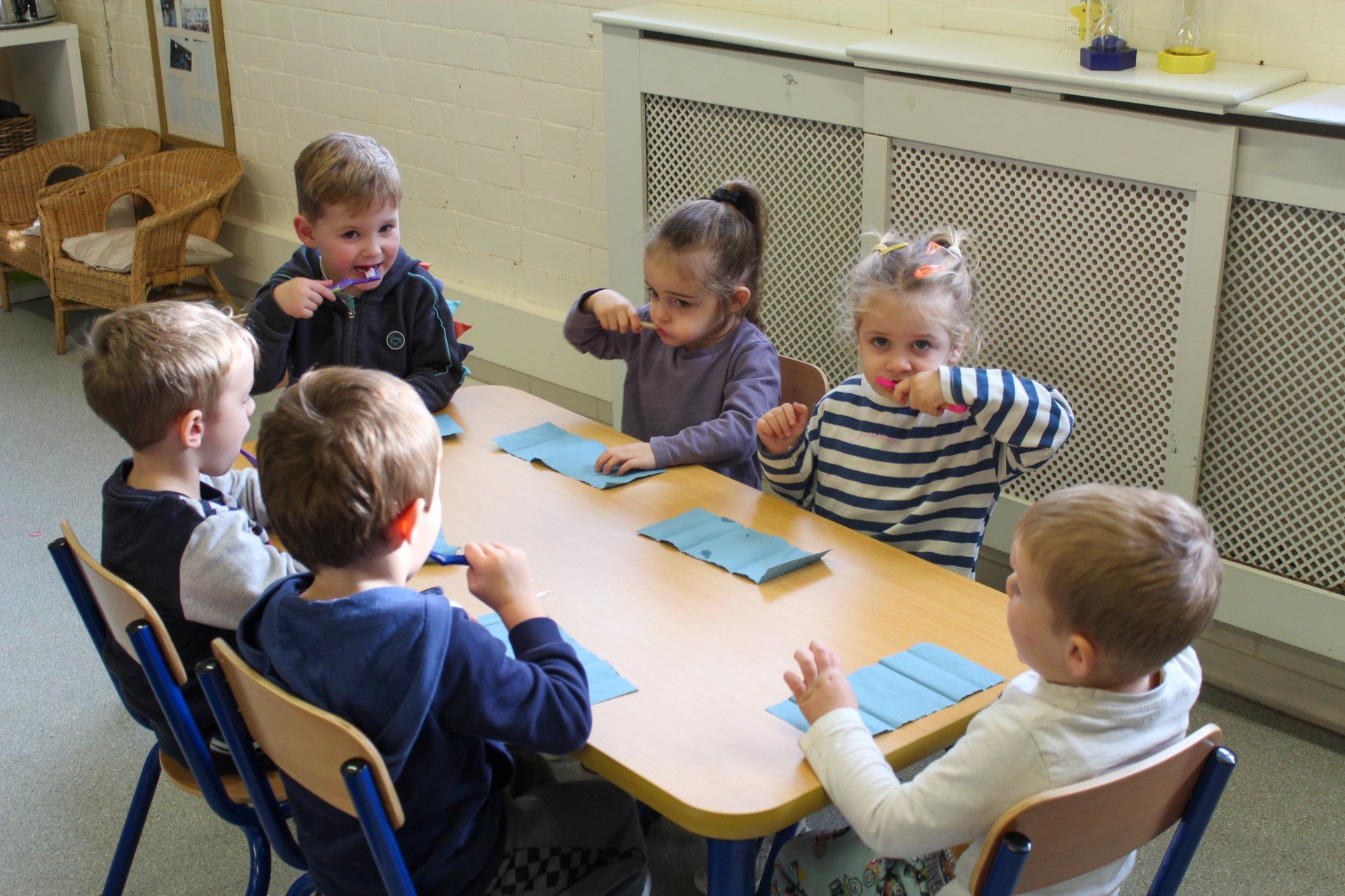 Children brushing their teeth around a table; a classroom setting.