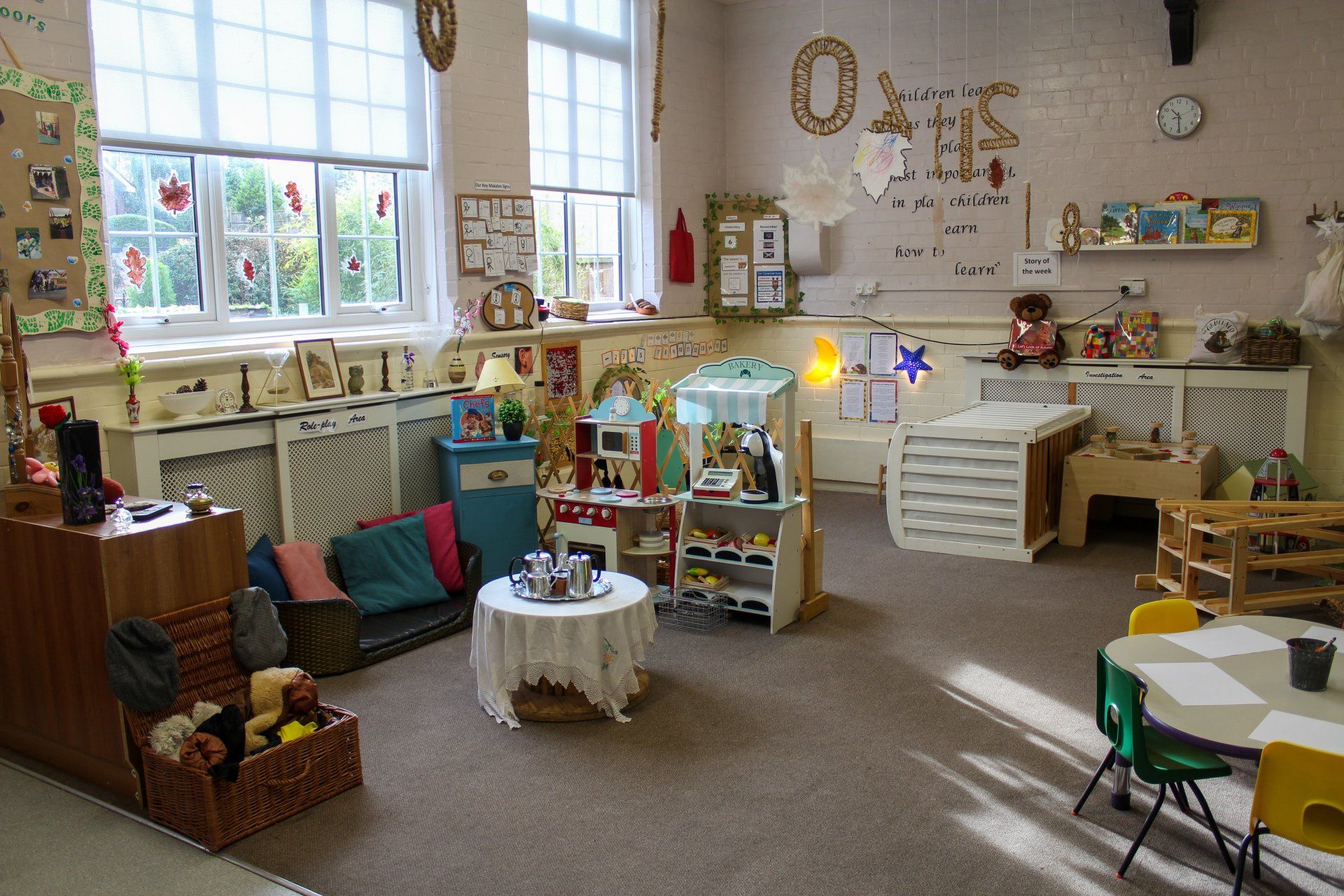 A child's playroom with various toys, seating areas, and a play kitchen near windows.