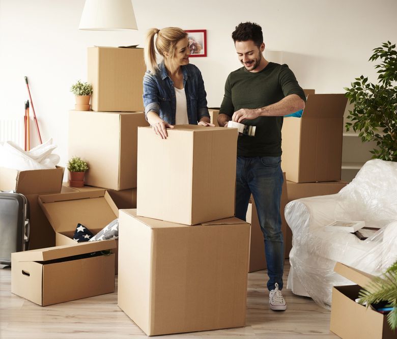 A Man and a Woman Are Packing Boxes in a Living Room — Johns Removals Newcastle In Rankin Park, NSW