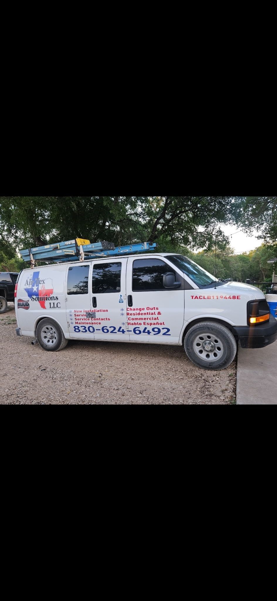 White service van parked on gravel, with kayaks on the roof rack. The van has signage, with a Texas flag.