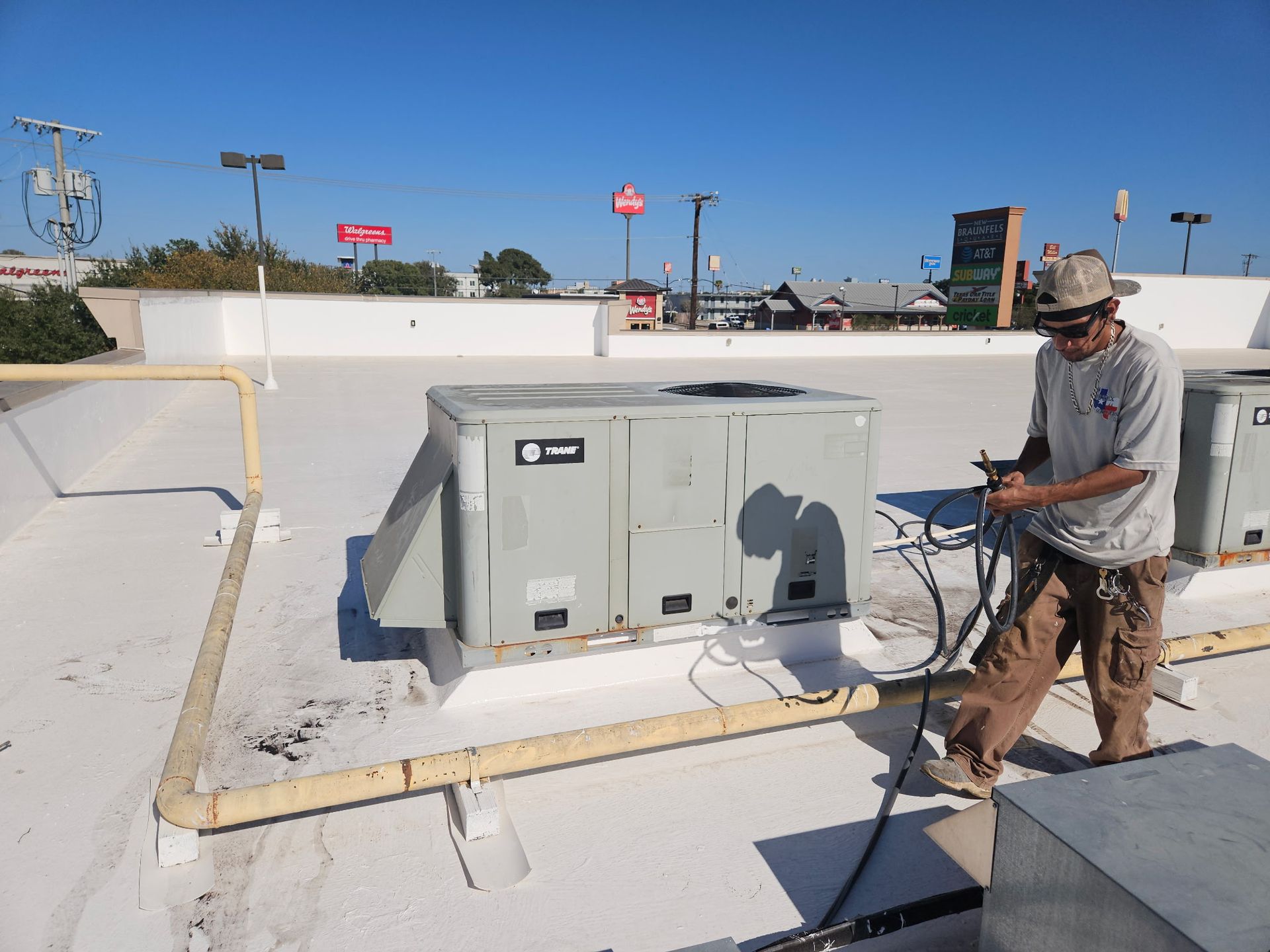 Man working on an HVAC unit on a white commercial rooftop; sunny day.