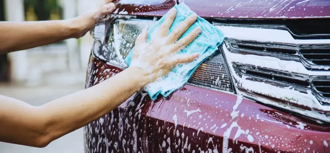 A person is washing a red car with a towel.