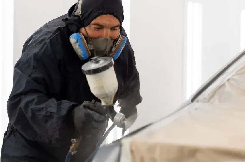 A man wearing a mask is spray painting a car.