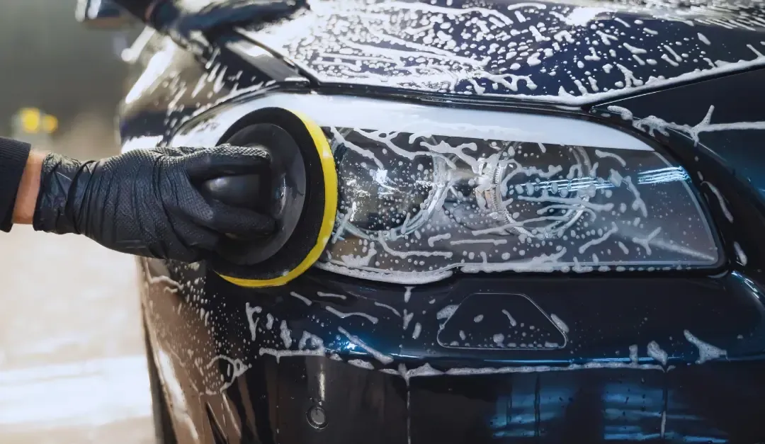 A person is polishing the headlight of a car.