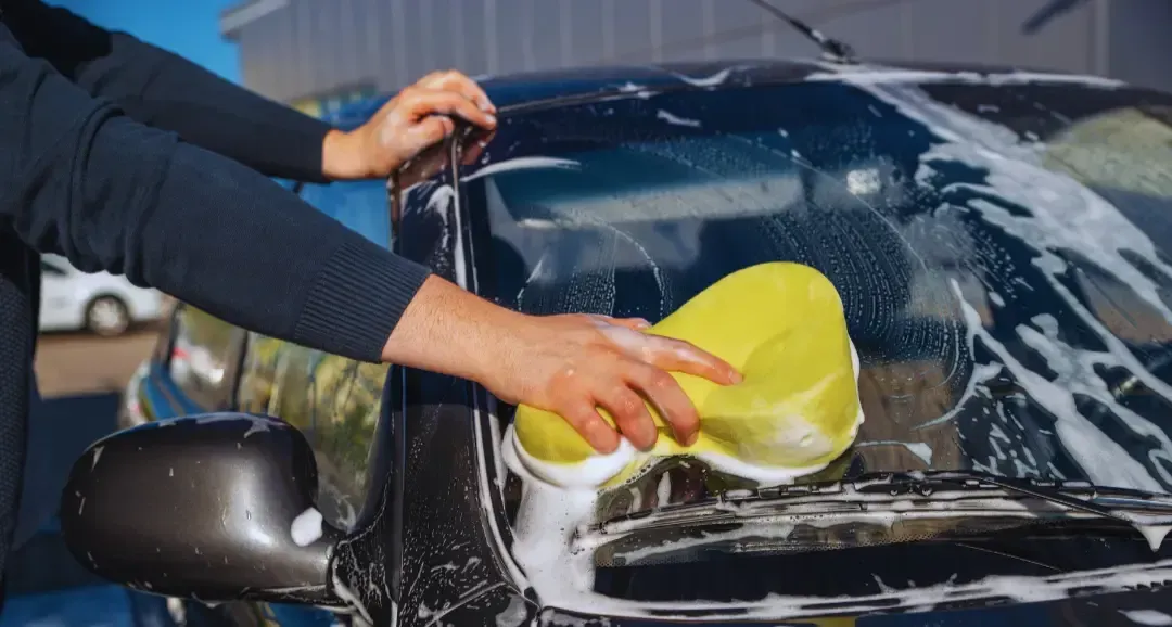 A person is washing a car with a yellow sponge.