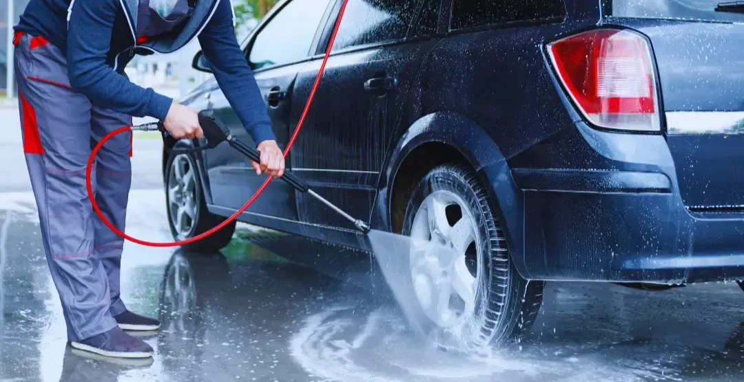 A man is washing a car with a high pressure washer.