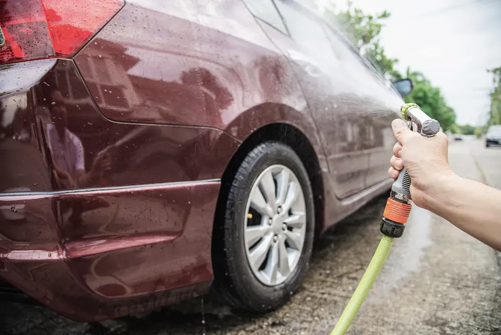 Mobile Detailing Services - A person is washing a car with a hose.