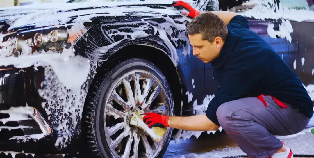 A man is kneeling down to wash a car.