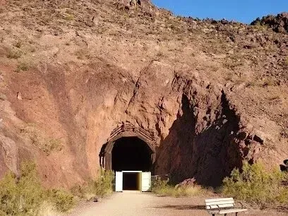 Mobile Detailing-Tunnel entrance carved into reddish-brown rock, with a paved path and a bench in the foreground.
