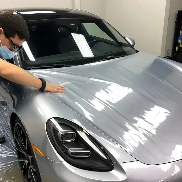 Ceramic Coating Mobile-Detailing-Man applying clear protective film to a silver Porsche car hood in a garage.