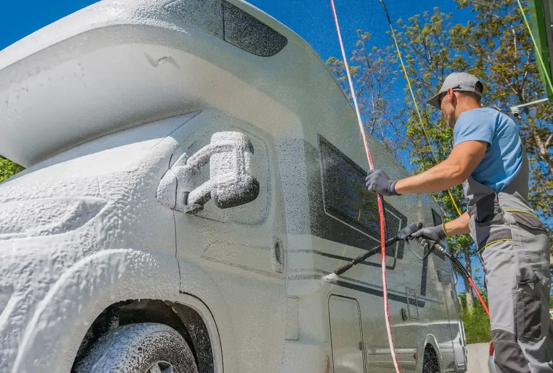 A man is washing a rv with foam and a hose.