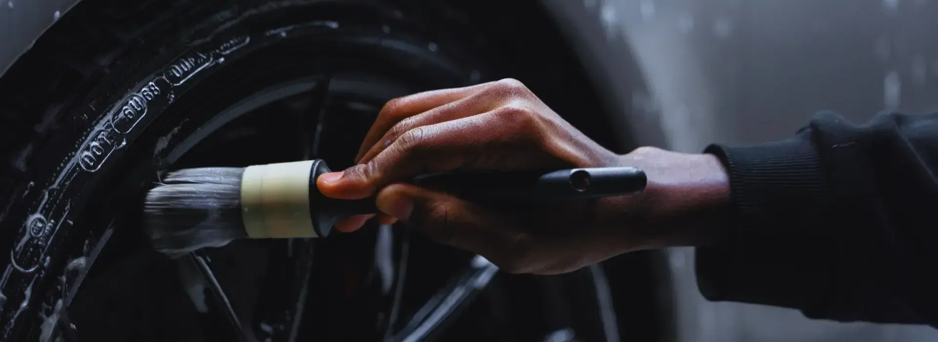 A person is cleaning a car wheel with a brush.