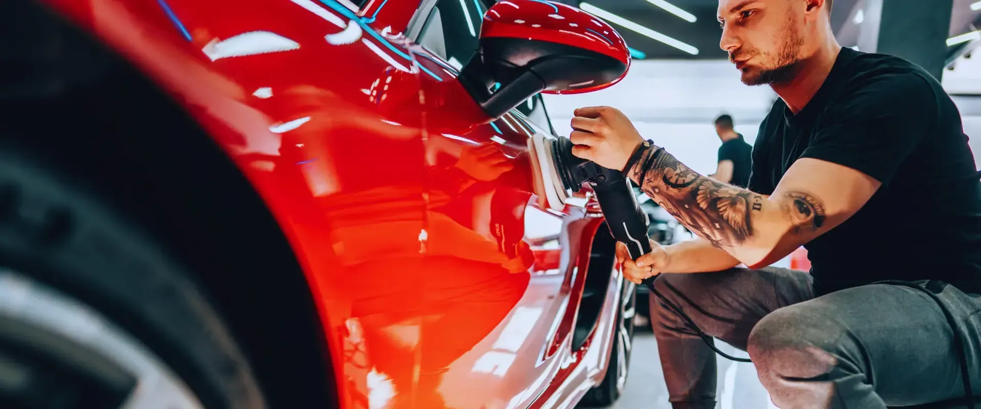 A man is kneeling down next to a red car.