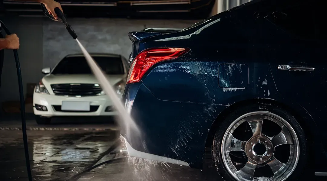 A man is washing a car with a high pressure washer.