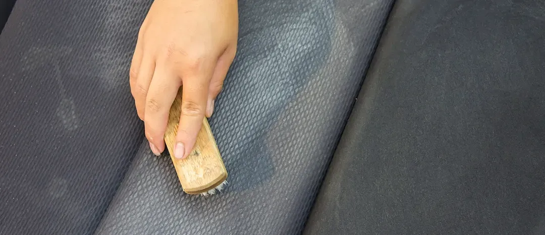 A person is cleaning a leather seat with a brush.