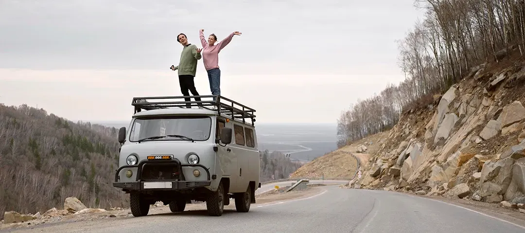 A man and a woman are standing on top of a van on a road.