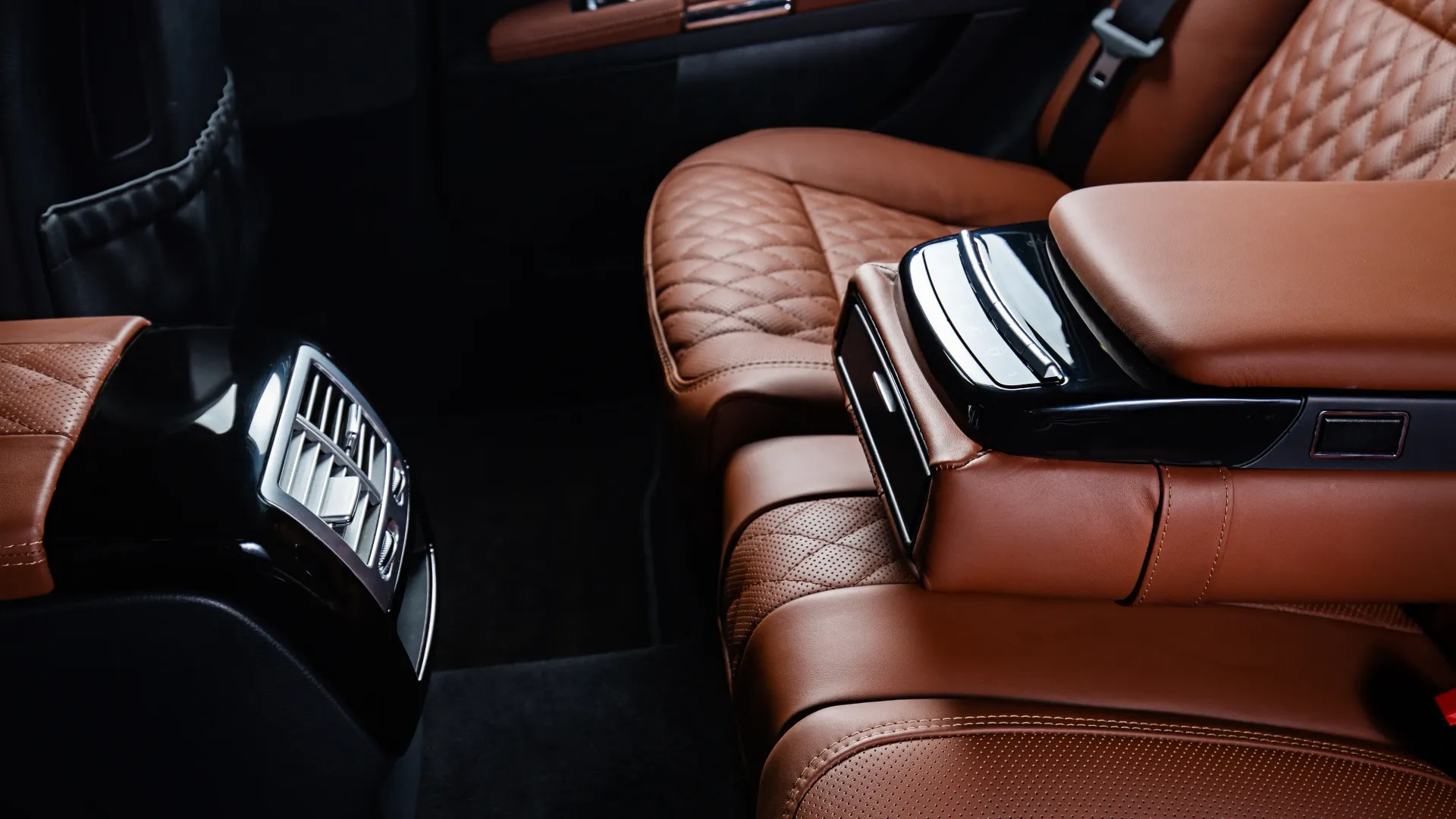 the back seat of a car with brown leather seats and a black arm rest .