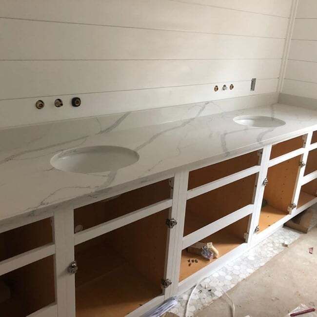 A bathroom counter with two sinks and white cabinets