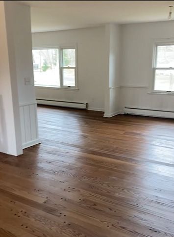 An empty living room with hardwood floors and white walls.