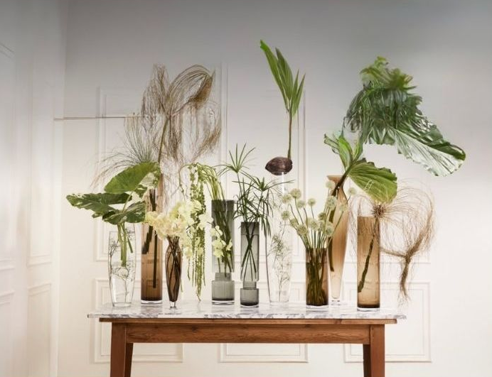 a wooden surface with glass vessels holding plants and flowers