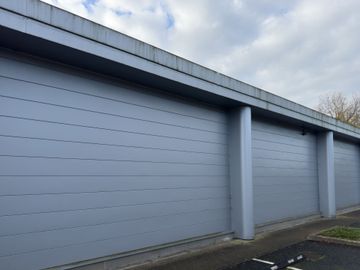 Gray building exterior with horizontal paneling and vertical supports under a cloudy sky.