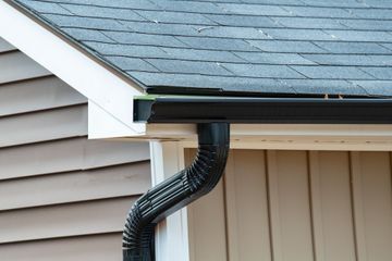 Black rain gutter on a house with gray roof and tan siding.