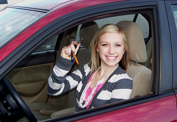 Smiling woman in a maroon car holding keys in the driver’s seat